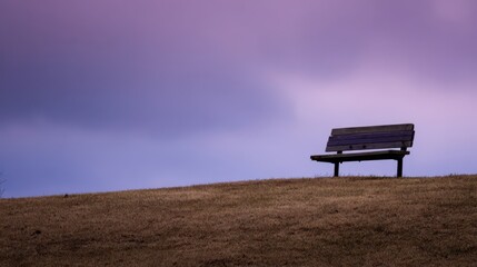 Fototapeta premium A solitary wooden park bench rests on a hilltop, bathed in a tranquil, purple-tinged twilight.