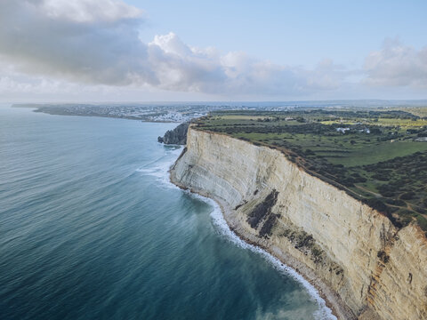 Aerial view of the rugged cliffs meet the turquoise sea in a dramatic display of nature's artistry, Praia do Porto de Mos, Lagos, Faro, Portugal.