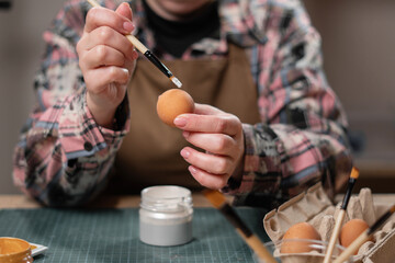 Easter eggs at home. Close-up of woman decorating painting easter egg using brushes. holiday creativity and festive preparation.