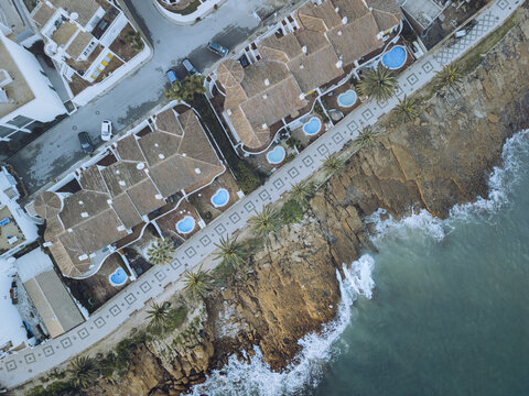 Aerial view of golden cliffs meeting turquoise waters, with neat rows of houses and pools lining the shore, Luz, Faro, Portugal.