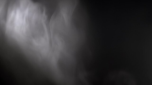 White smoke cloud swirls and drifts from the left side of the frame. Soft directional light highlights the ethereal texture against a solid black background.