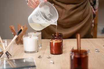 Naklejka premium Creative hobby as Handmade soy wax candle in workshop. Close-up of woman pouring liquid wax into the mold.