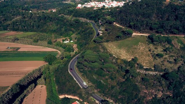 Drone view of a winding road in a mountainous area with moving cars.  Cinematic look. Aerial view of a beautiful hilly area with a highway.  Cars are driving in a scenic area, top view.