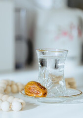 Water in a glass, a date and a rosary on a white table.