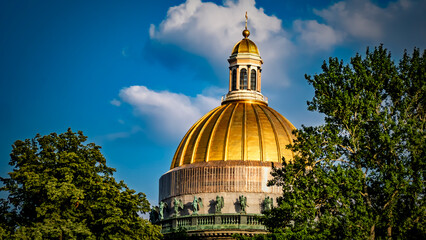 Two golden church domes with crosses tower over buildings and trees under a cloudy blue sky. The urban landscape of ST. PETERSBURG with power lines.