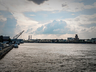 Dramatic river view with city skyline under stormy clouds. A pier extends into the water, featuring a crane boats. Moody lighting creates a striking scene