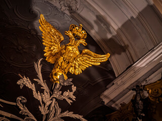 A stunning golden double-headed eagle sculpture adorns an ornate interior archway. Detailed carvings dramatic lighting highlight its regal presence