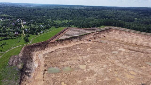Expansive drone footage of a sand quarry, slowly encroaching on a tranquil village and lush forests. Aerial view of industrial mining, raw earth, and excavation site