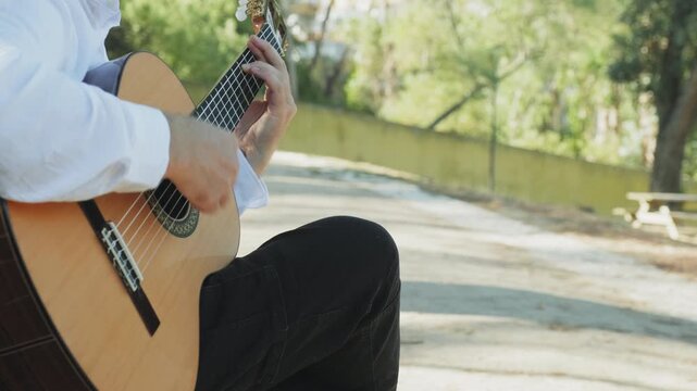 Professional guitarist plays guitar outdoors. Musician plays a classical guitar in the park. A man in a white shirt plays a musical instrument outside the house. The guitarist plays the guitar.