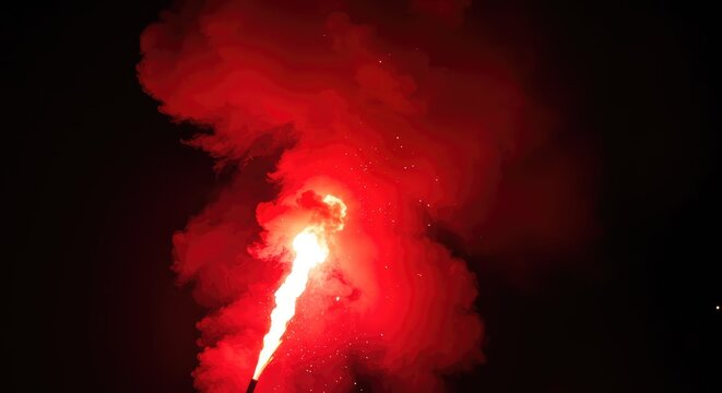 A vibrant red chemical flare burning intensely, emitting dense smoke and brilliant sparks into the dark atmosphere during a nighttime celebration or signal ,texture ,hot ,rescue