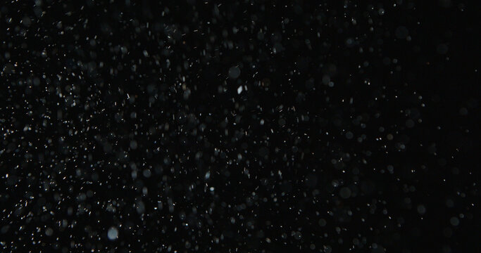 Tiny snow or dust randomly flying in the smoky air, empty space template for objects advertisement. Many dust particles cloud of white powder in low light on empty dark black contrast background.