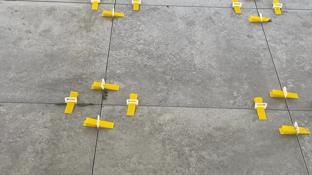Tile leveling system on concrete floor, showing yellow spacers for precise installation