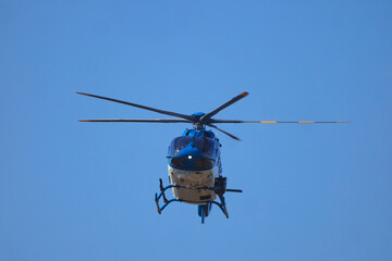 Fototapeta premium Blue and white helicopter inflight on patrol against clear blue sky. 