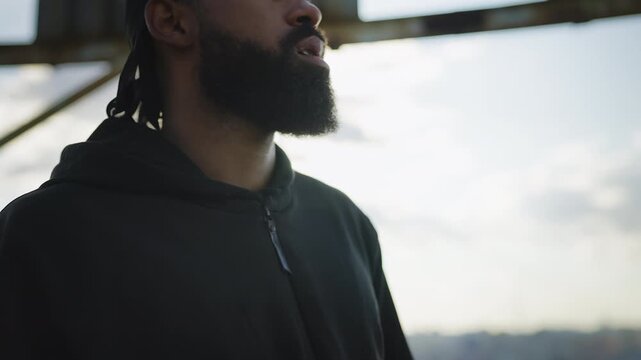 Black male in hoodie and durag smoking cigarette on rooftop, stress relief