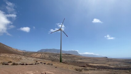 Wind turbine generating electricity in a rugged desert landscape, symbolizing renewable energy and environmental sustainability under a clear blue sky © DawDunia