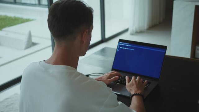 Programmer typing code on laptop in home office in natural light. Coding and software development remote work scene as programmer focuses on security code hands on keyboard in minimalist workspace.