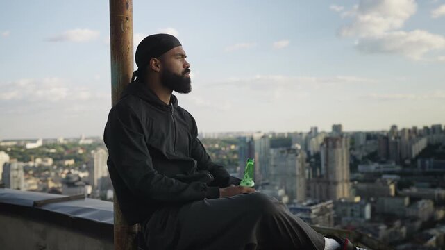 African American man drinking beer while enjoying cityscape from rooftop edge