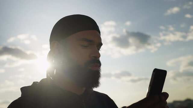 Young African American man typing message on phone on rooftop, arranging meeting