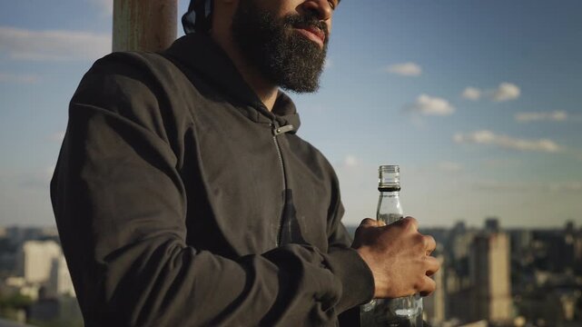 Young African American male drinking alcohol on rooftop, coping with stress