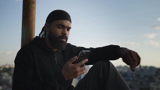 Young man wearing durag texting client on phone, selling marijuana online