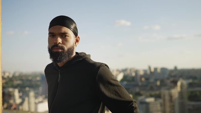Portrait of upset Black male in durag standing alone on rooftop, troubled life