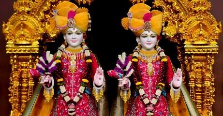 Obraz premium Beautiful close-up view of indian god swaminarayan face glowing, smile and blessing idols. isolated blurry pink designed costume and yellow crown, black curtain and gold interior view in background.