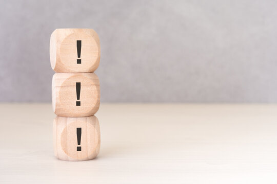 Vertical stack of wooden cubes with exclamation mark symbols, concept of attention and warning. Conceptual pair with question marks available in portfolio.