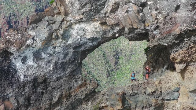 Hiking couple sitting inside El Bujero rock cave overlooking Los Gigantes cliffs and Masca Valley in Tenerife