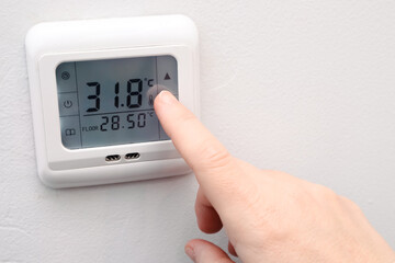 Hand adjusting temperature on a digital wall thermostat for underfloor heating.