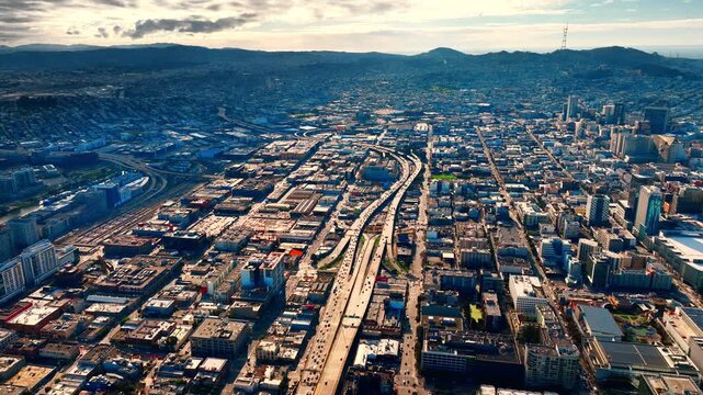 High angle aerial view looking down at a interstate 80 intersection cutting through the urban landscape of San Francisco. Dense buildings and residential areas surround the infrastructure.