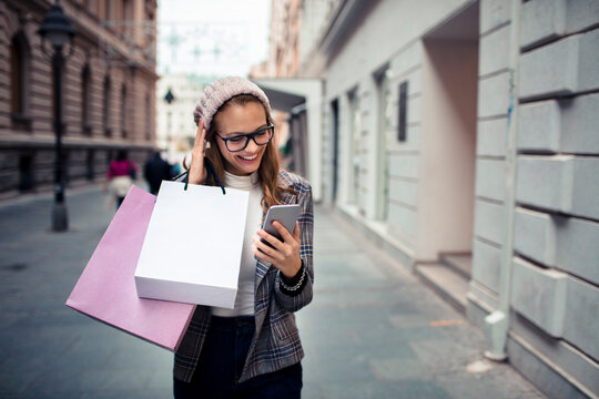Smiling woman shopping with smartphone on city street