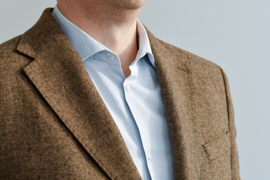 Close up of businessman wearing brown tweed blazer with light blue shirt, with a collar fragment. Selective focus.