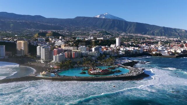 Cinematic aerial sunrise over Puerto de la Cruz cityscape with Lago Marti&aacute;nez and Teide volcano in Tenerife