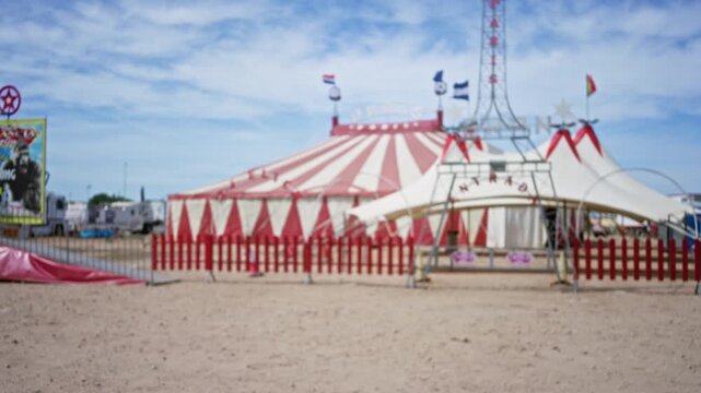 Blurred red and white circus tent bokeh background in an outdoor setting with soft defocused fence and sky; template overlay virtual production.