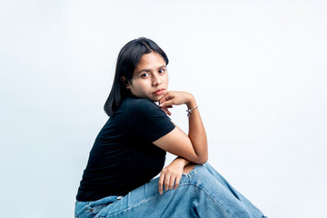 Side profile portrait of a beautiful young woman sitting on a white floor, resting her chin on her hand with a calm and confident gaze. © Ryan