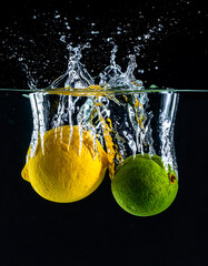 Citrus fruits plunge into water, creating splash with dark background