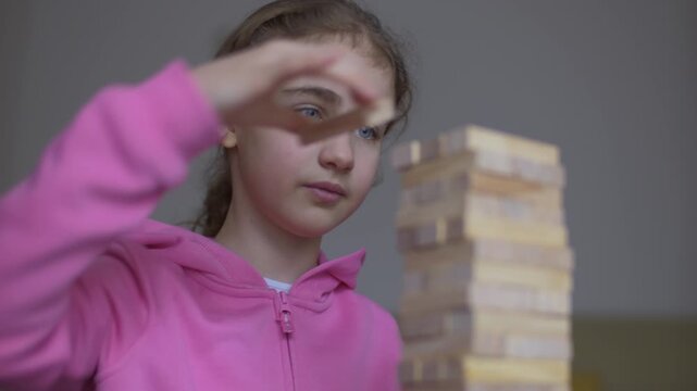 Child Having Fun Building Constructor Tower of Wooden Blocks. Girl Playing Wooden Block Tower Game at Home. Board Creative Game. Child Development Education Leisure. Play With Wooden Building Blocks.