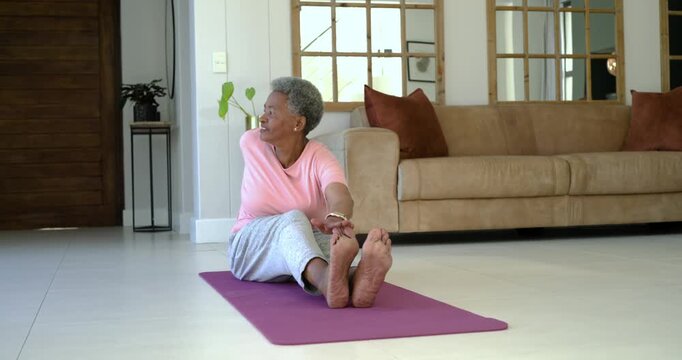 Senior African woman stretching on purple yoga mat in living room, alternating bends and twists