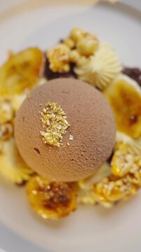 A dessert with a chocolate ball on top and a bunch of nuts around it. The dessert is served on a white plate