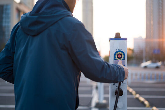 Man operating a Hikvision electric vehicle charging station in an urban setting at dusk