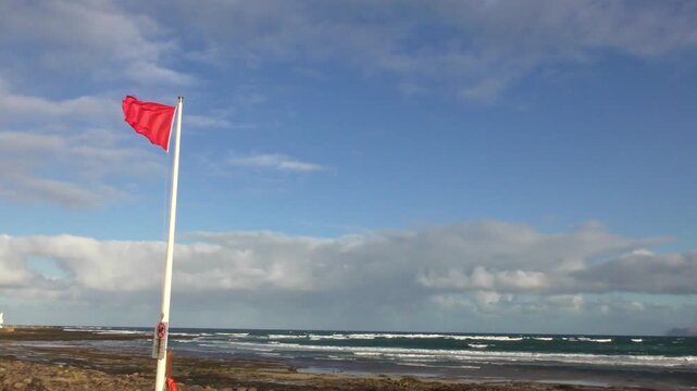 Rote Flagge flattert im starken Wind - Badeverbot am Strand, Sturm, Strandsicherheit, gef&auml;hrliche Bedingungen, Windrichtung, K&uuml;ste, Wassersport, Warnsignal f&uuml;r Schwimmer, Surfen, Sommerurlaub, Strand