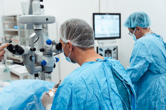 Professional ophthalmologists conducting a micro-invasive eye procedure in a sterile operating room using clinical blue drapes and high-tech equipment.
