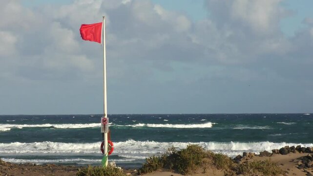 Red flag fluttering in strong wind - swimming ban, warning signal for swimmers on the beach, storm, beach safety, dangerous conditions, wind force, wind direction,  weather forecast, coast