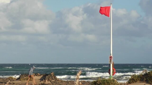 Red flag fluttering in strong wind - swimming ban, warning signal for swimmers on the beach, storm, beach safety, dangerous conditions, wind force, wind direction,  weather forecast, coast