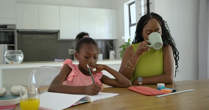 African American mother and daughter at table writing schoolwork with pencil looking up mom helping
