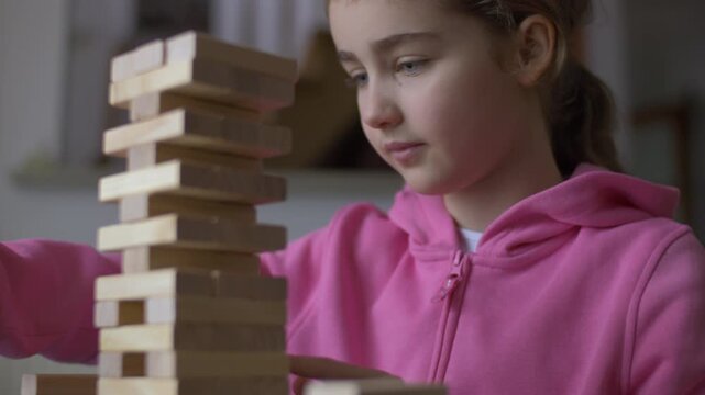 Child Having Fun Building Constructor Tower of Wooden Blocks. Girl Playing Wooden Block Tower Game at Home. Board Creative Game. Child Development Education Leisure. Play With Wooden Building Blocks.