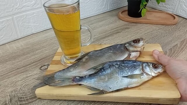 There is draft beer and dried fish on a wooden board on the table