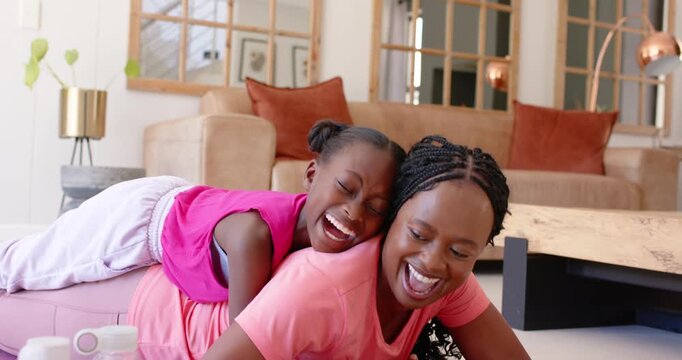 African mom and daughter, child climbing onto mom's back on ottoman laughing and cuddling at home