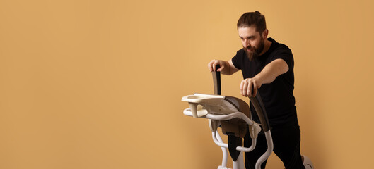 Bearded man in black sportswear using an elliptical machine on a neutral beige background, demonstrating an active and healthy lifestyle.