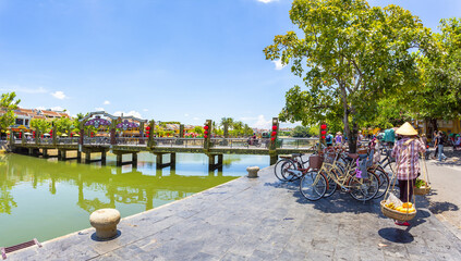 Vietnamese fruit vendor woman wearing a conical hat carrying baskets of tropical fruit in Hoi An